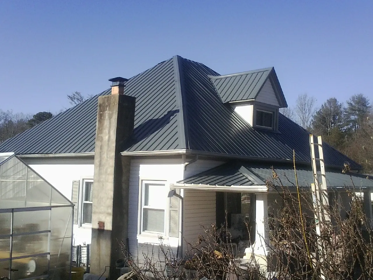 Dark blue standing seam metal roof on a white farmhouse with dormer — Slate & Tile Roof Repair by Roofing Brothers in South Dayton