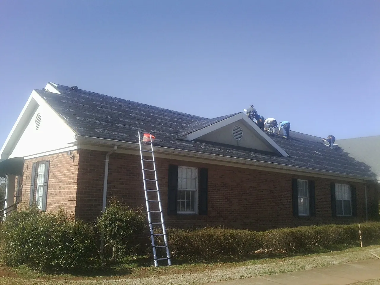 Crew tearing shingles off a brick ranch roof with a ladder set — Emergency Roof Repair work by our crew in South Dayton