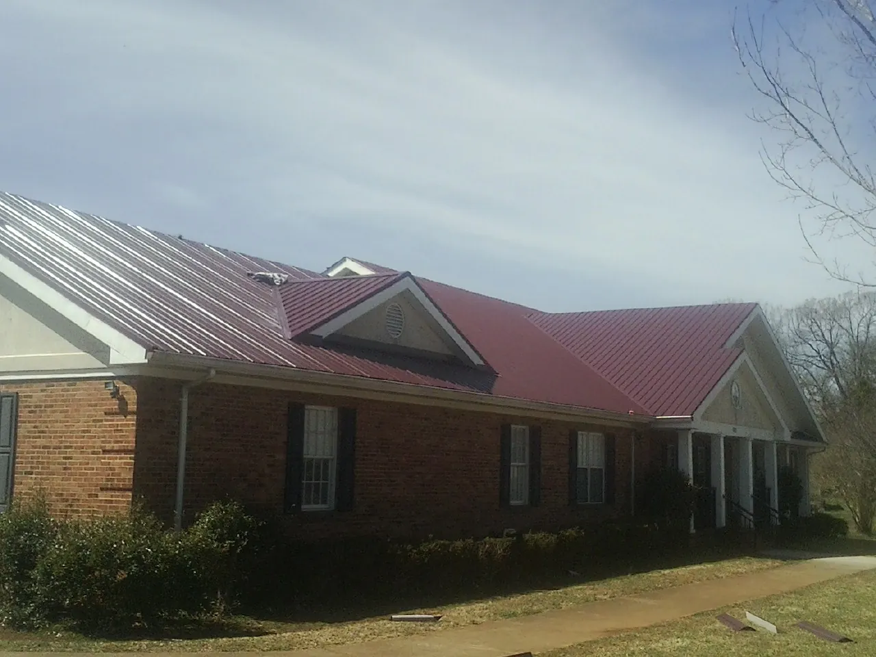 Red metal roof with gabled entries on a long brick building, from a Hail Damage Roof Repair job in South Dayton