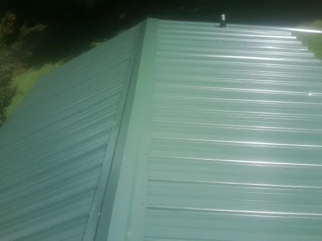 New green metal panels meeting at the ridge of a roof — Flat Roof Repair work by our crew in South Dayton