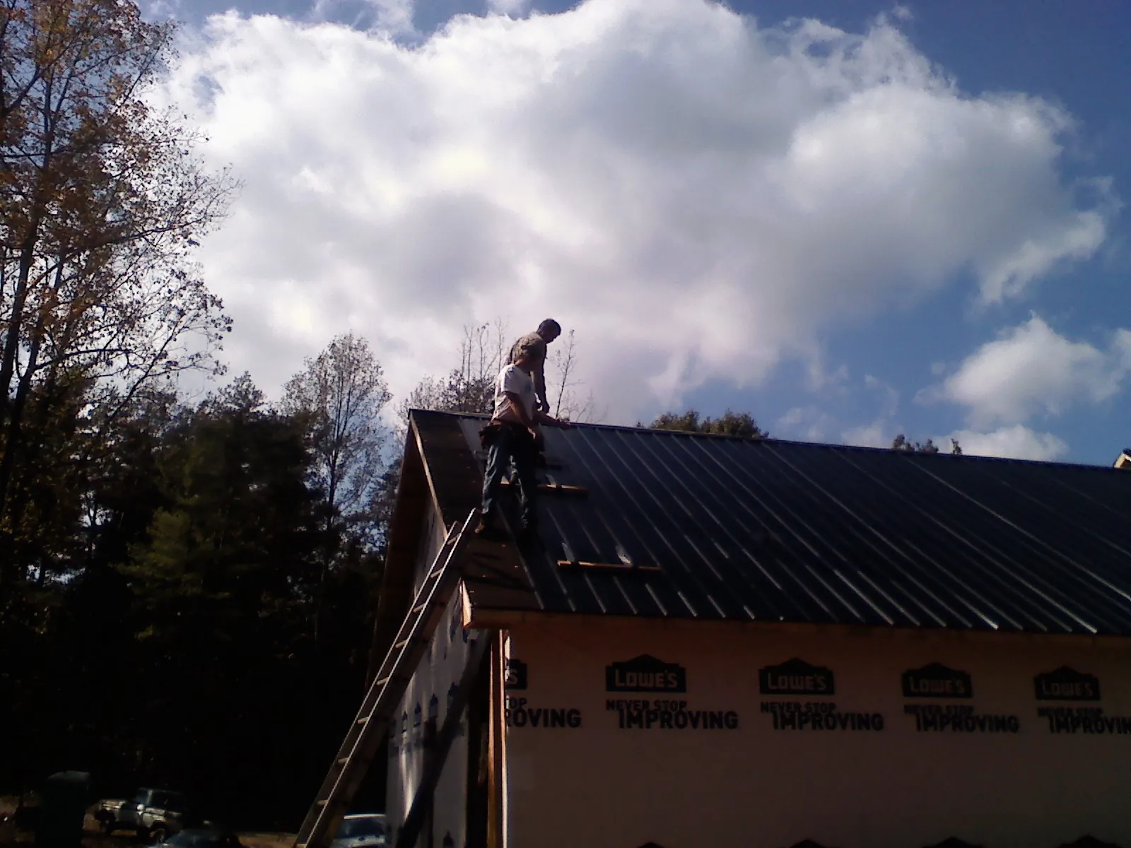 Roofer fastening dark metal panels high against a cloudy sky, from a Roof Inspection job in South Dayton