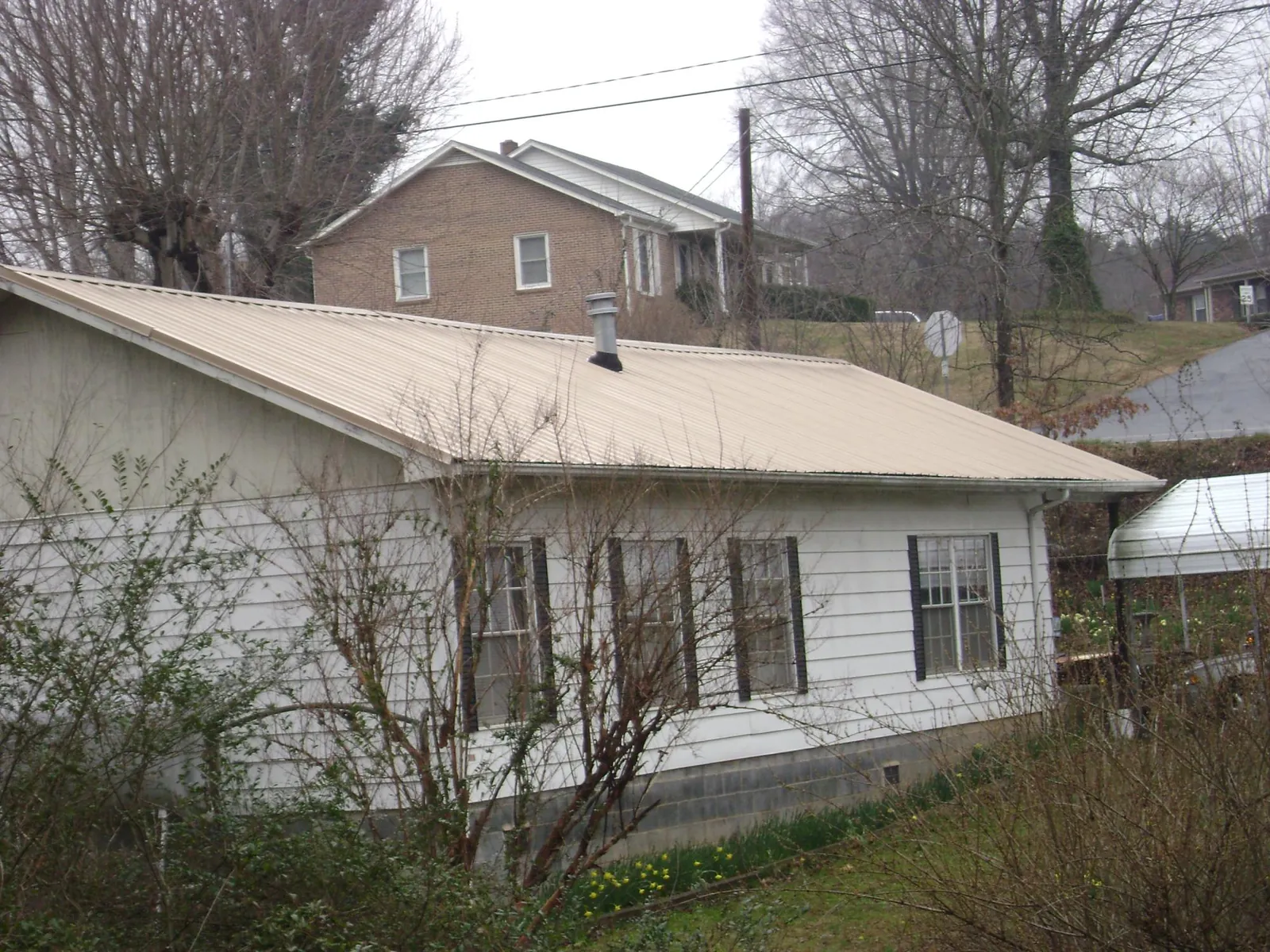 Tan metal roof on a white sided house set into a hillside — Commercial Roofing by Roofing Brothers in South Dayton